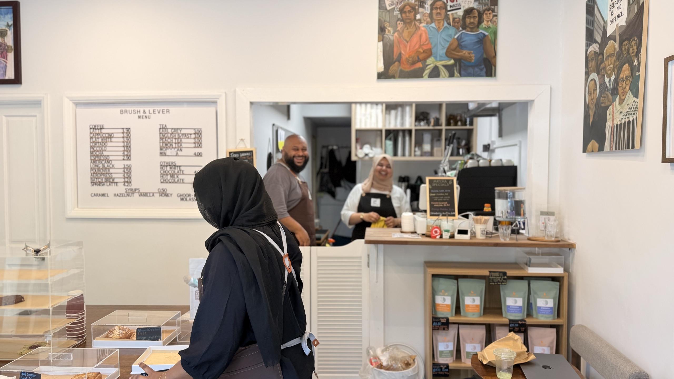 Inside Brush & Lever — two staff behind the counter beneath the menu board and framed paintings